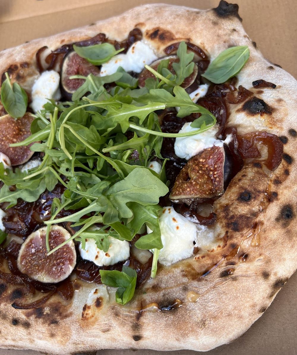 Close-up of the Figgi Smalls pizza: fresh figs, goats cheese, caramelised red onion, basil and wild rocket on a charred crust